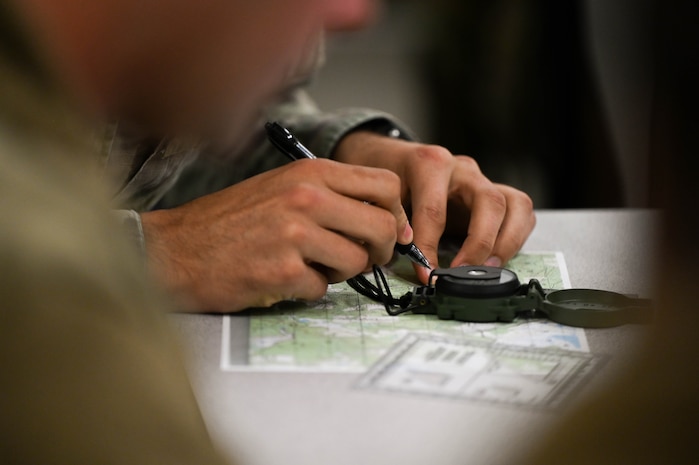 An airman uses a map and a compass as he learns land navigation during BATTLE school.