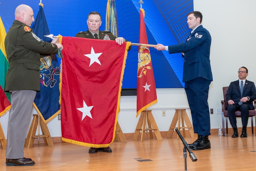 Maj. Gen. John Pippy, center, and Command Sgt. Maj. Shawn Phillips, left, unfurl Pippy's two-star flag during a ceremony Feb. 28, 2025, at Fort Indiantown Gap, Pa. During the ceremony, Pippy was sworn in as Pennsylvania’s 55th adjutant general and promoted to his current rank. (Pennsylvania National Guard photo by Wayne V. Hall)