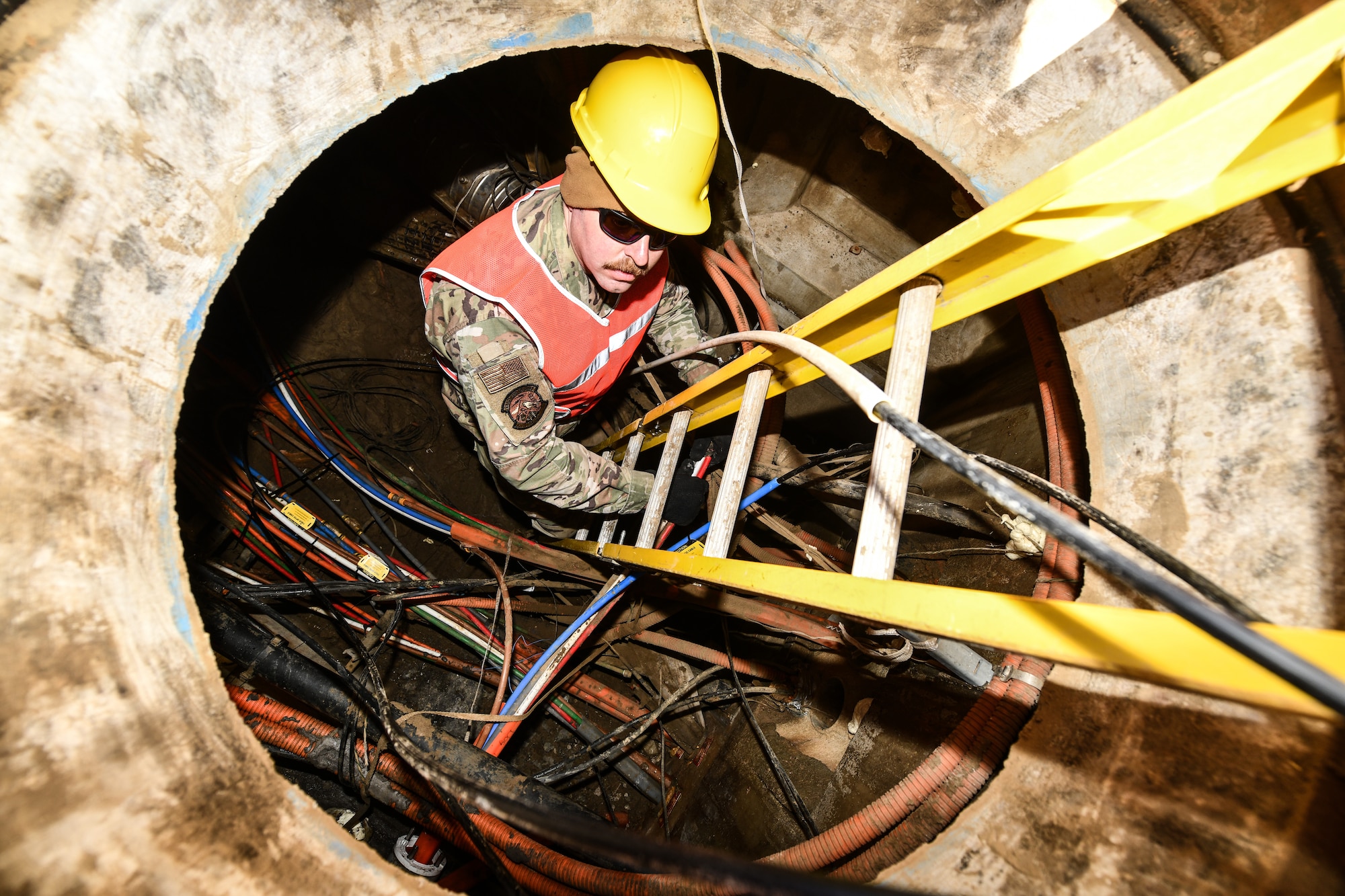 Airman 1st Class Eric Castonguay, 243rd Eingineering and Installation Squadron, Maine Air National Guard, climbs up from a manhole housing fiber optic cable on Offutt Air Force Base, Jan. 29, 2025. the 243rd EIS layed 5000 feet of fiber optic cable to connect the new construction projects on the base.(U.S. Air Force photo by Chad Watkins)