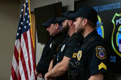 Three men dressed in police uniforms look to the right toward an American flag.