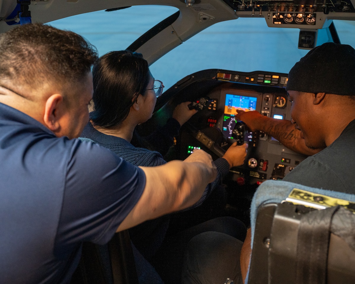 Airmen sit in the cockpit of a T-1A Jayhawk simulator while being guided by retired Col Andy "Gatos" Katz, at Laughlin Air Force Base, Texas, Dec. 17, 2024. To honor the legacy of the T-1A Jayhawk, Airmen took part in red carpet simulators, being able to practice flying the T-1. (U.S. Air Force photo by Staff Sgt. Nicholas Larsen)