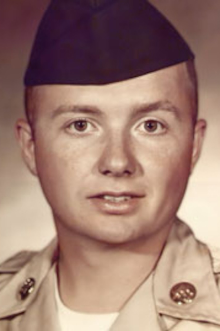 A man poses for a portrait photo wearing combat uniform.