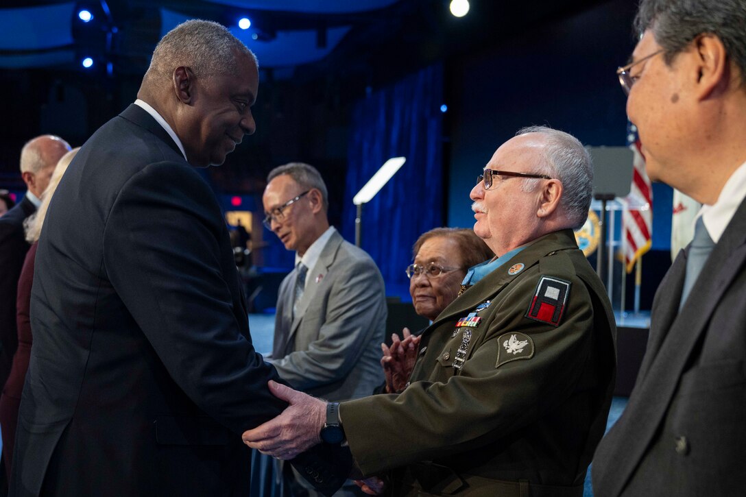 Secretary of Defense Lloyd J. Austin III shakes hands with a Medal of Honor recipient while others observe.