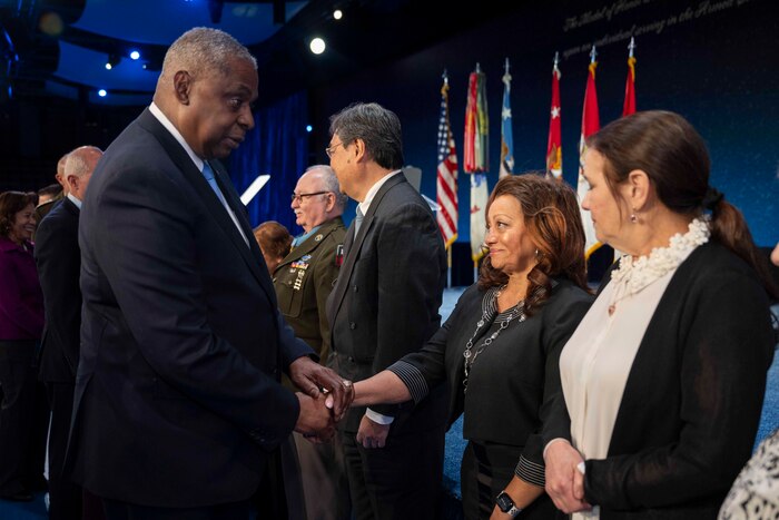 Secretary of Defense Lloyd J. Austin III shakes hands with one of several civilians.