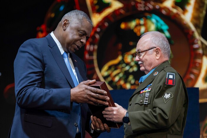 Secretary of Defense Lloyd J. Austin III presents a framed flag to a Medal of Honor recipient.