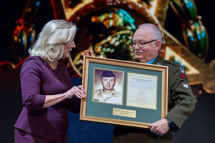 An Army leader presents a framed citation to a Medal of Honor recipient.