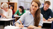 A female NSA employee sitting at a desk in a classroom taking notes during class