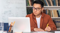 An Asian NSA employee taking notes from their laptop during their college course