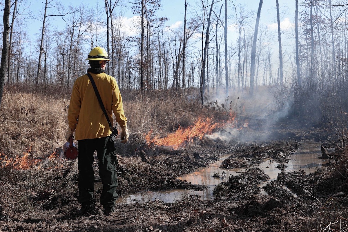 A firefighter wearing wildland fire gear manages a fire.