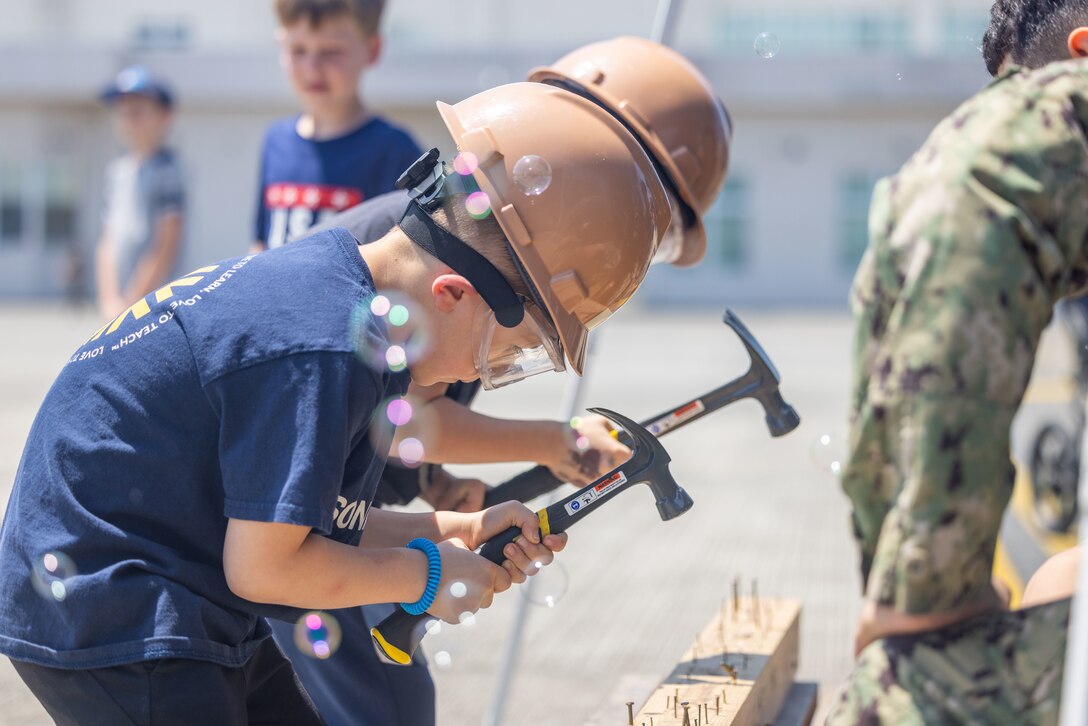 Students from Marine Corps Air Station Iwakuni hammer nails into a board during a construction demonstration hosted by Sailors assigned to Headquarters and Headquarters Squadron, MCAS Iwakuni, and Sailors assigned to Naval Construction Battalion 4, Thirtieth Naval Construction Battalion, during a Science, Technology, Engineering and Mathematics (STEM) day at MCAS Iwakuni, Japan, May 3, 2024.  U.S. Marines, Sailors, and civilians along with Japan Maritime Self-Defense Force members displayed equipment and held interactive demonstrations to teach children about STEM-related careers. (U.S. Marine Corps photo by Cpl. Calah Thompson)