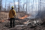 A firefighter wearing wildland fire gear manages a fire.