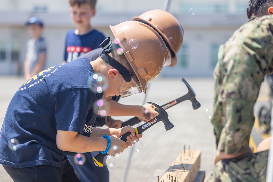 Students from Marine Corps Air Station Iwakuni hammer nails into a board during a construction demonstration hosted by Sailors assigned to Headquarters and Headquarters Squadron, MCAS Iwakuni, and Sailors assigned to Naval Construction Battalion 4, Thirtieth Naval Construction Battalion, during a Science, Technology, Engineering and Mathematics (STEM) day at MCAS Iwakuni, Japan, May 3, 2024.  U.S. Marines, Sailors, and civilians along with Japan Maritime Self-Defense Force members displayed equipment and held interactive demonstrations to teach children about STEM-related careers. (U.S. Marine Corps photo by Cpl. Calah Thompson)