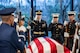 Service members from each branch of the armed forces are saluting and holding rifles in front of their chests while surrounding the flag-draped casket of former President Jimmy Carter.