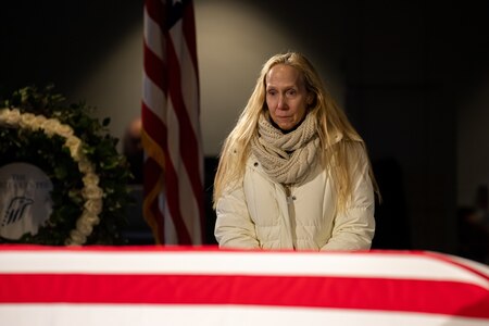 A woman wearing a scarf and white cost looks at the flag-draped casket of former President Jimmy Carter.