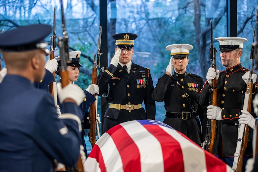 Service members in dress uniforms salute a casket draped with an American flag.