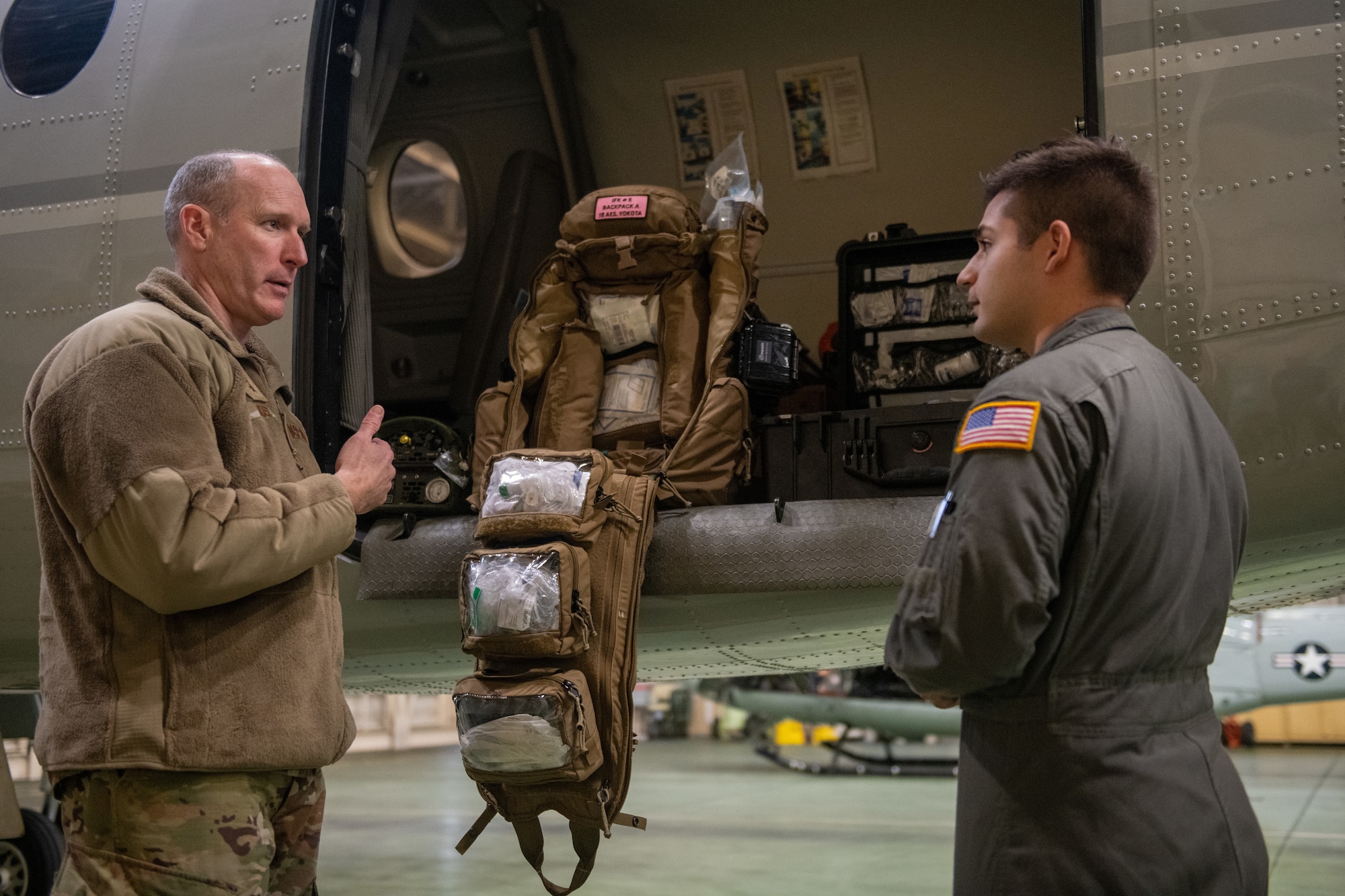 Two Air Force personnel engage in conversation standing beside an aircraft.