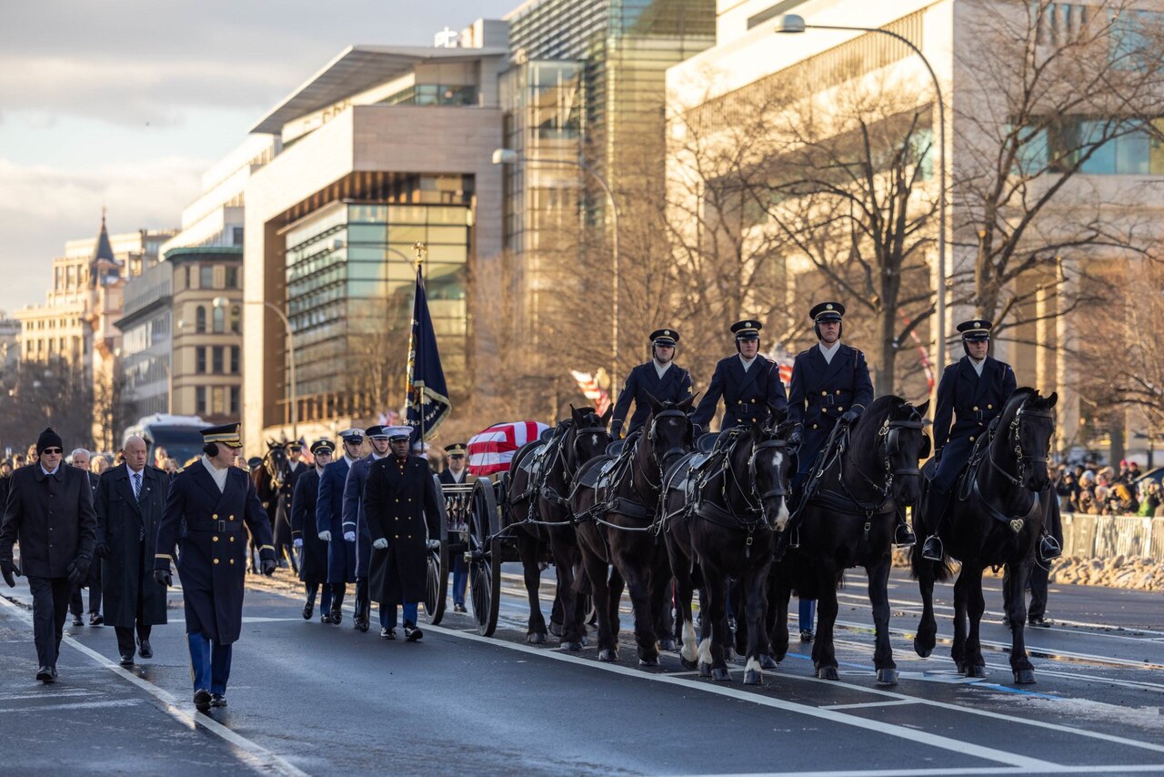 Soldiers on horseback, wearing winter dress uniforms, pull a caisson loaded with a flag-draped casket down a city street.