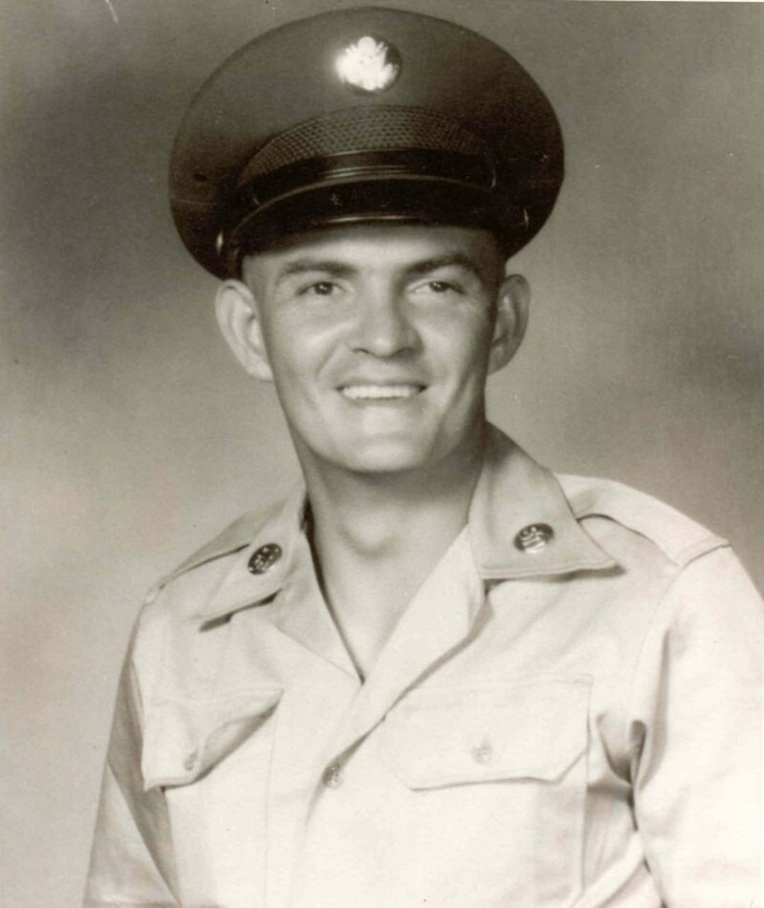 A man in uniform and cap smiles for a photo.