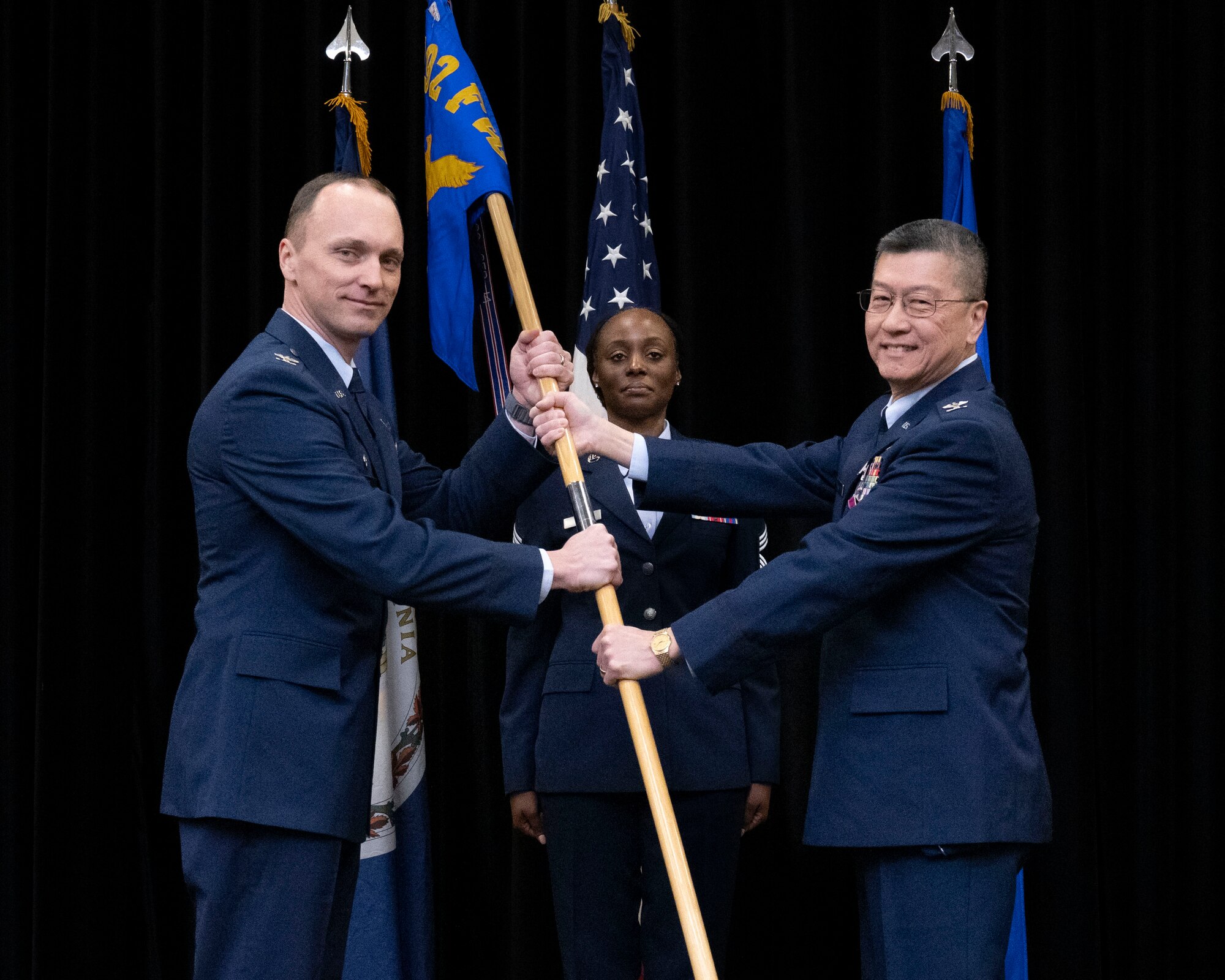 Two Air Force members holding 192nd MDG guidon with member in the background.