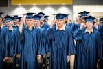 a large group of teenagers in royal blue graduation gowns and hats move their hat tassels to symbolize graduating.