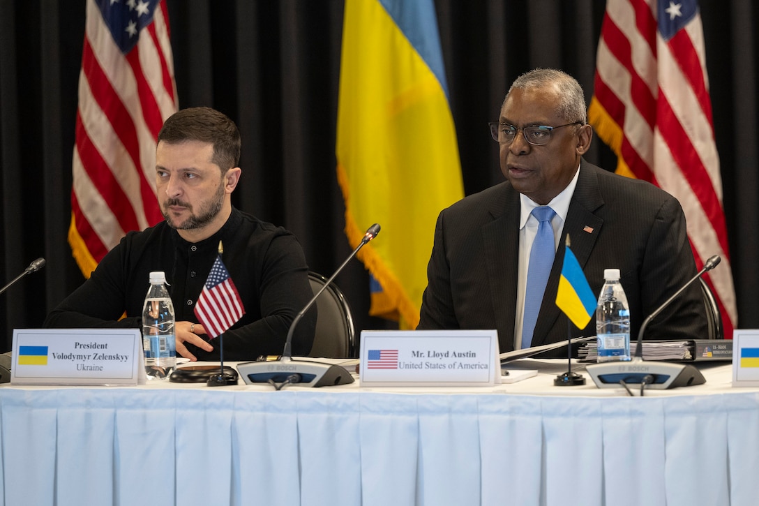 Secretary of Defense Lloyd J. Austin III speaks while sitting  at a table adorned with U.S. and Ukrainian flags next to the Ukrainian president.