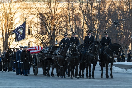 Army soldiers on horseback, wearing winter dress uniforms, pull a caisson loaded with a flag-draped casket down a city street.