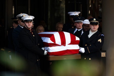 Multiple uniformed service members carry a flag-draped casket.