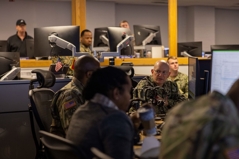 Service members in utility uniforms sit at the desks in an operations center.