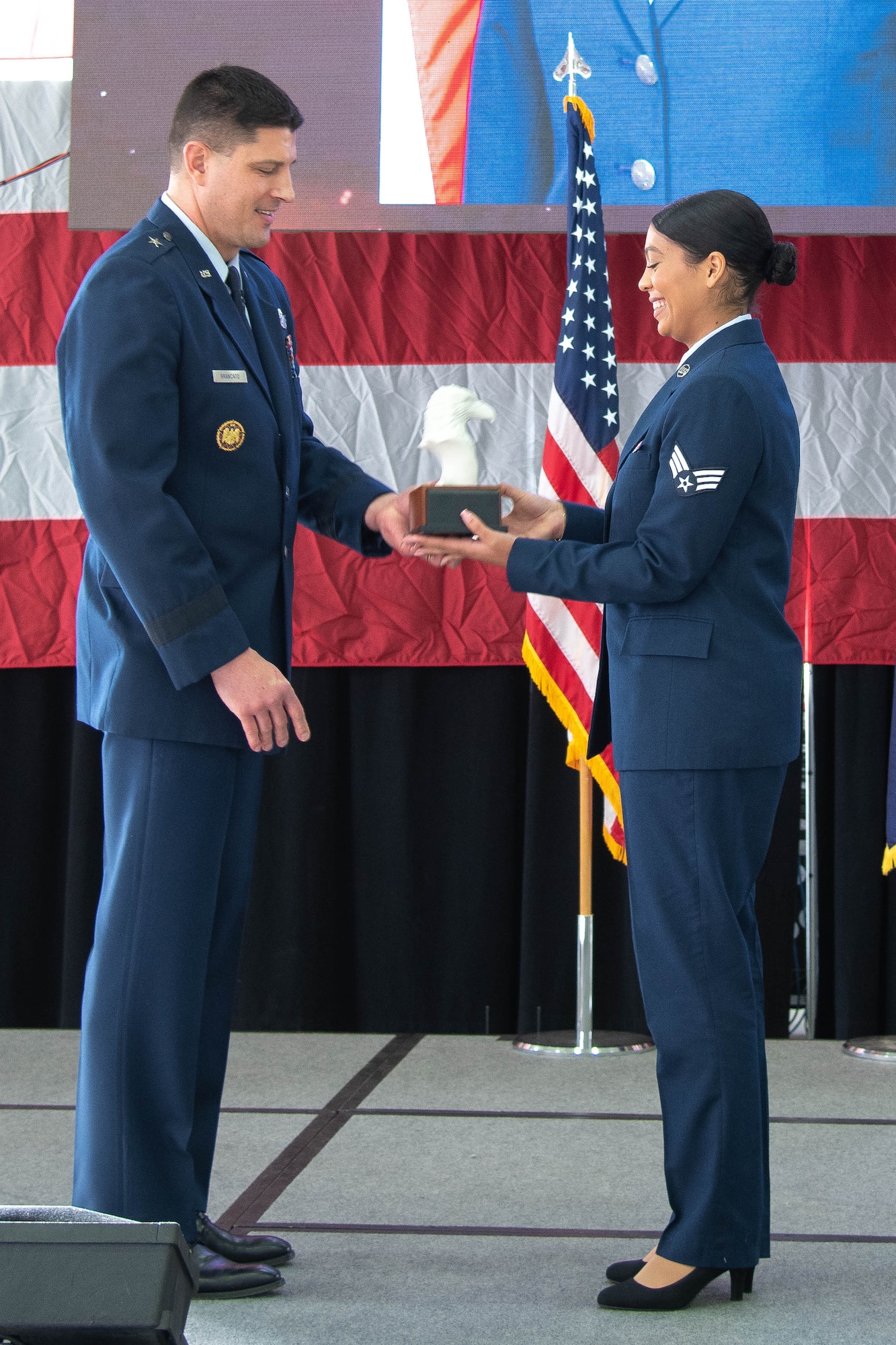 Male Air Force officer in blue dress uniform hands trophy to female junior enlisted Airman in dress uniform.