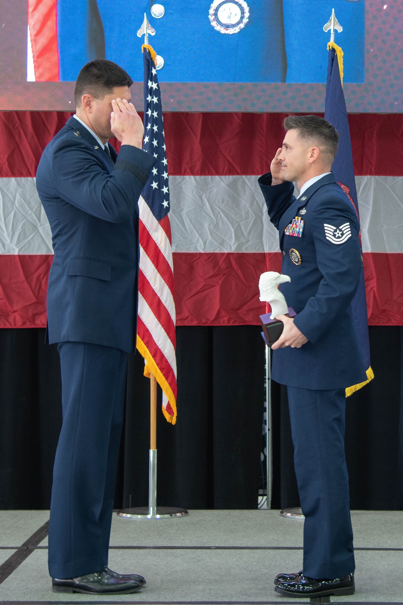 Side view of Air Force officer left, saluting Air Force non-commissioned officer, right, both are dressed in dress blue uniform.