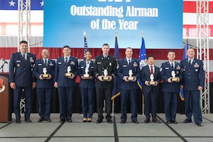 Line of nine Air Force and civilian stand while holding trophies. Air Force officer and senior enlisted leader flank each side respectively.