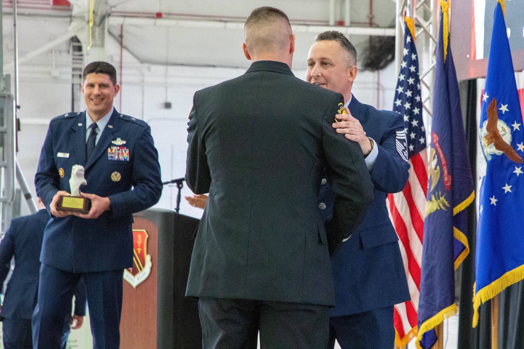 Air Force senior enlisted leader congratulates fire fighter in black dress uniform while air force officer looks on in background, holding trophy.