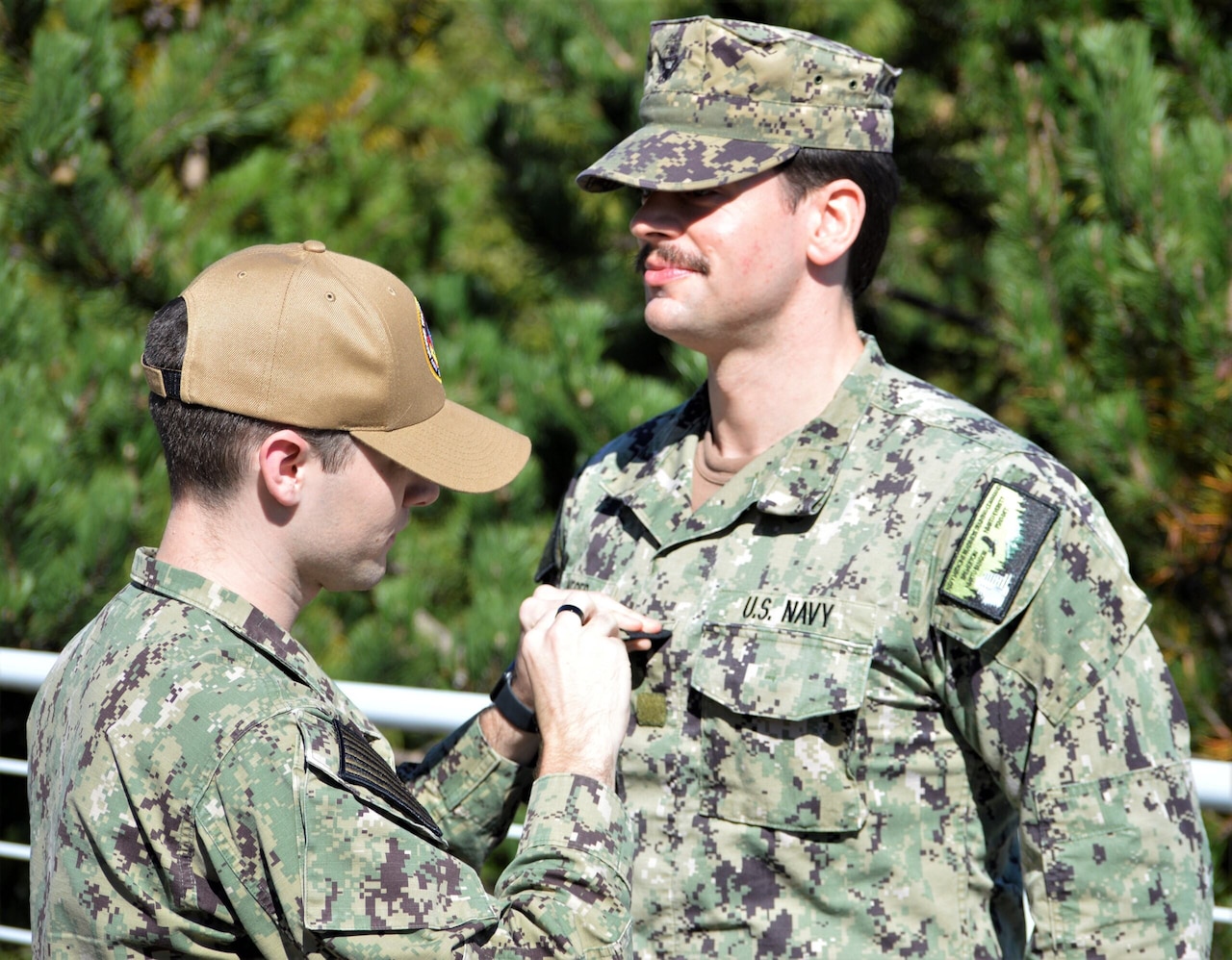 A man pins something to another man’s lapel.