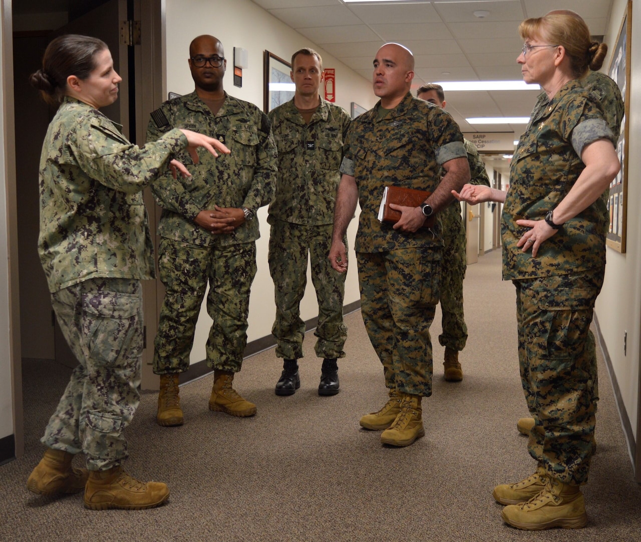 A group of people in military uniforms stand together in a hallway to talk.