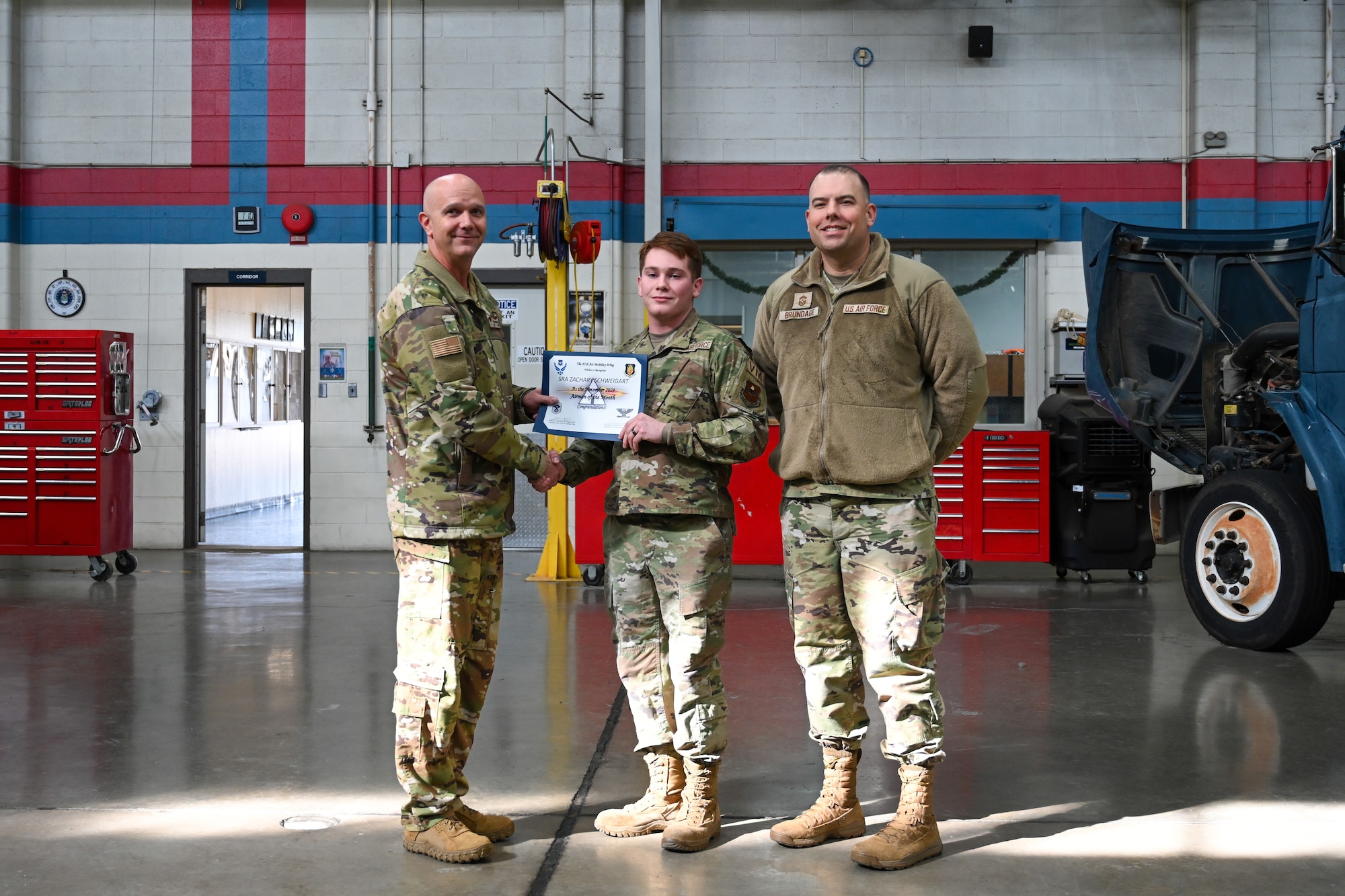 From left to right, U.S. Air Force Col. Jeff Marshall, 97th Air Mobility Wing (AMW) commander, Senior Airman Zachary Schweigart, 97th Logistics Readiness Squadron fire truck and refueler mechanic, and Chief Master Sgt. Justin Brundage, 97th AMW command chief, pose for a photo in the vehicle management shop at Altus Air Force Base, Oklahoma, Jan. 7, 2025. Schweigart was awarded the ‘Airman of the Month’ for November of 2024. (U.S. Air Force photo by Airman 1st Class Lauren Torres)