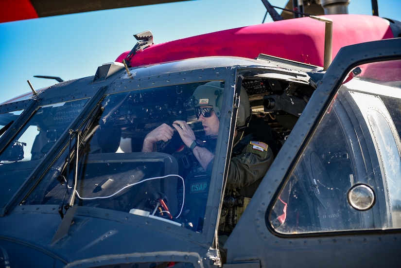 A service member is seated in the cockpit of a helicopter.