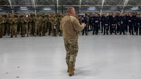 Photo of a U.S. Air Force service member in the foreground briefing hundreds of service members in the background inside a hangar.