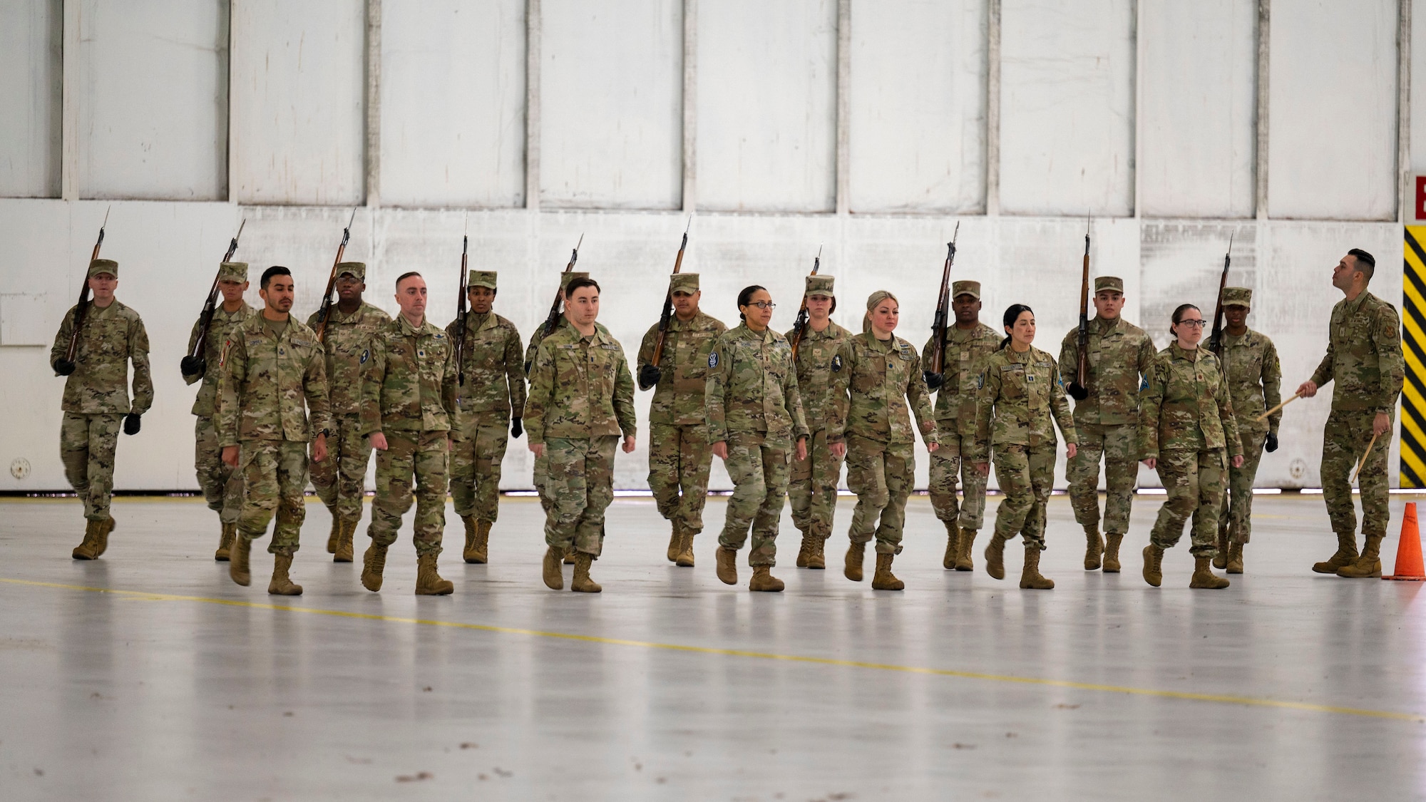 Photo of a U.S. Air Force Airmen and U.S. Space Force Guardians practicing marching movements inside a military hangar.