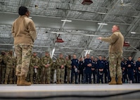 Photo of a U.S. Air Force Airman in the foreground briefing hundreds of service members in the background inside a hangar.