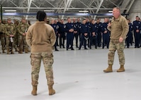 Photo of a U.S. Air Force Airman in the foreground briefing hundreds of service members in the background inside a hangar.