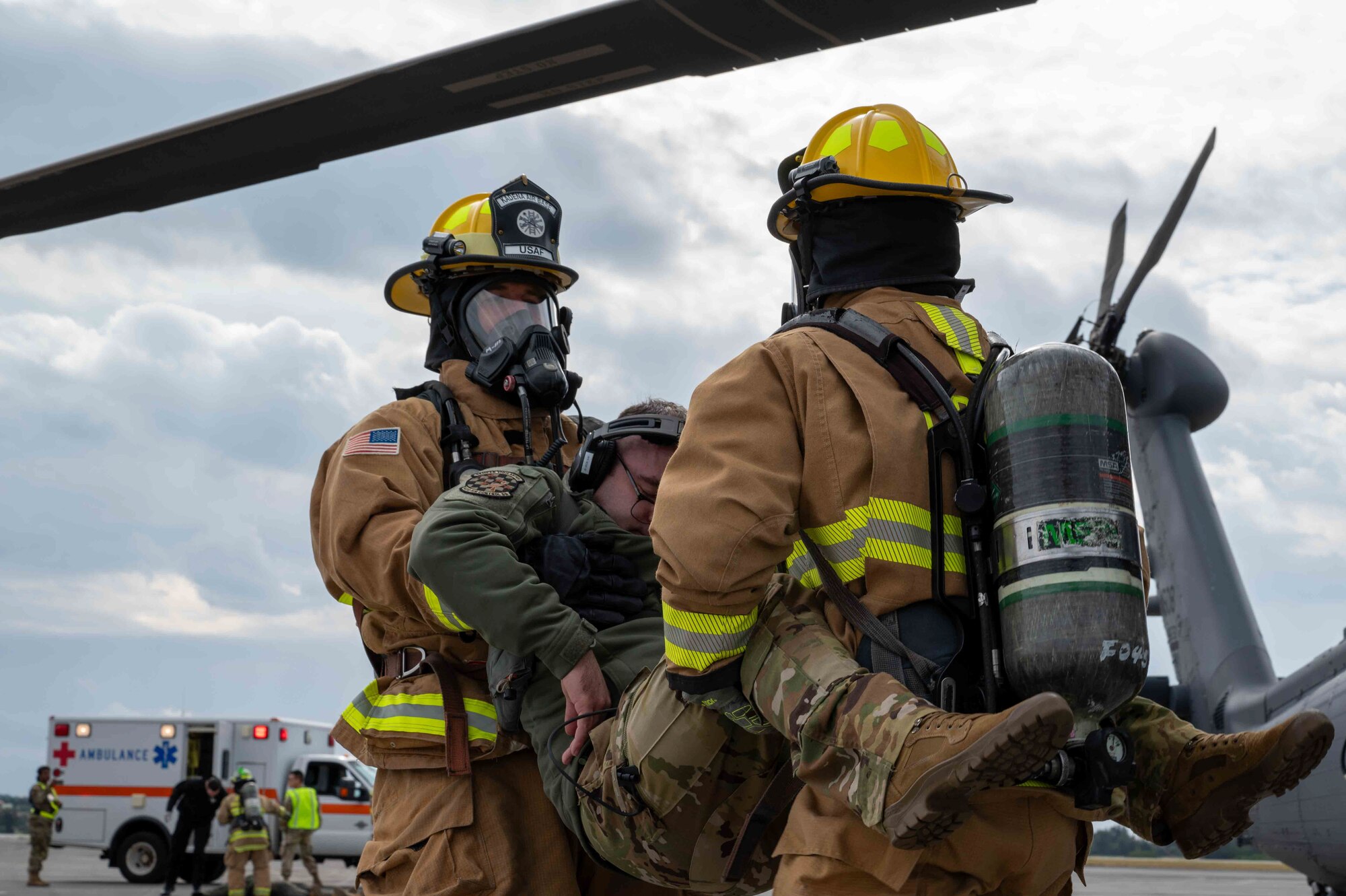 Two service member firefighters are carrying another service member that's simulated to be to be out cold