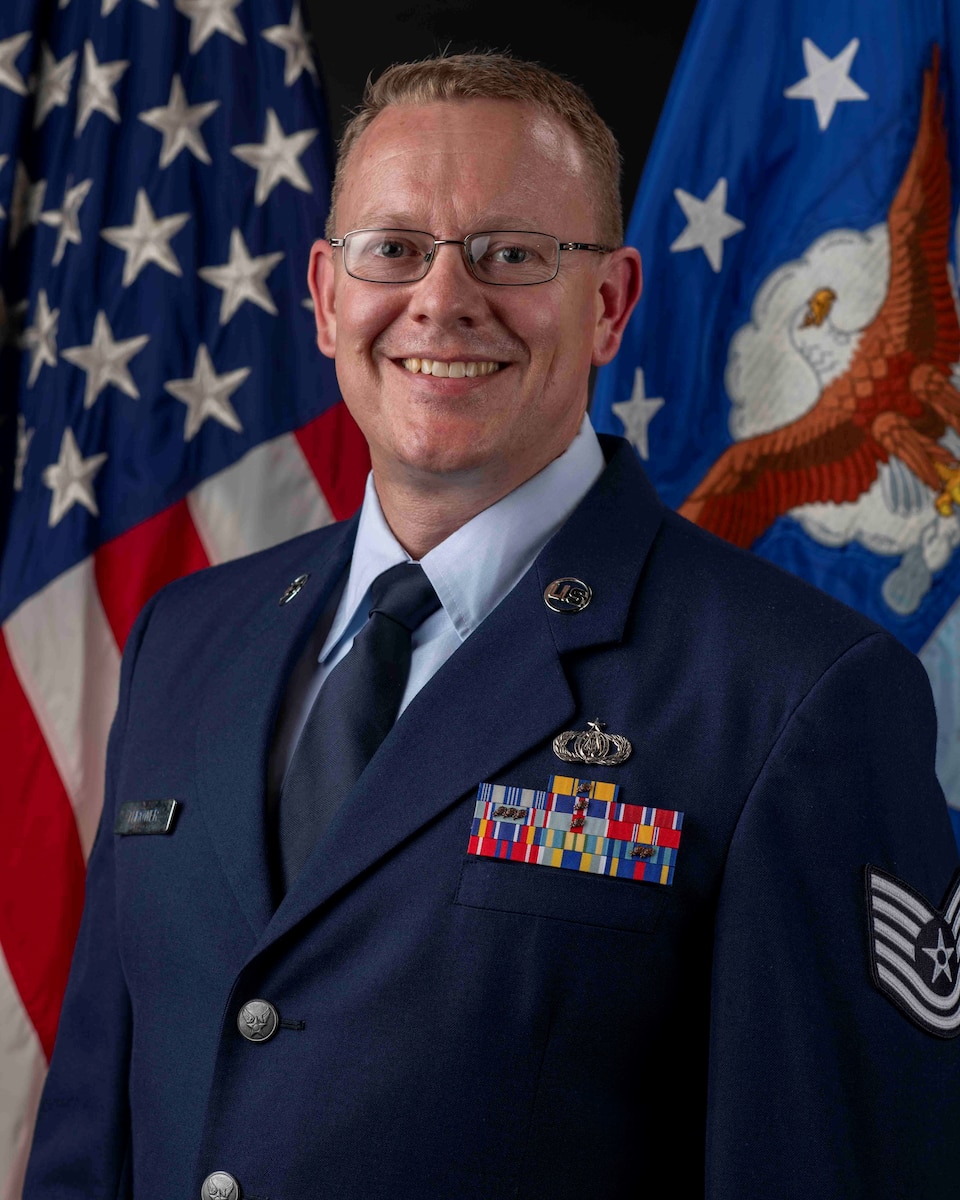 Official Photo of TSgt Daniel Thrower, regional band trumpet with the USAF Band of the Pacific-Asia, Yokota AB, Japan.  TSgt Thrower is wearing blue service dress in front of the US and USAF flags.
