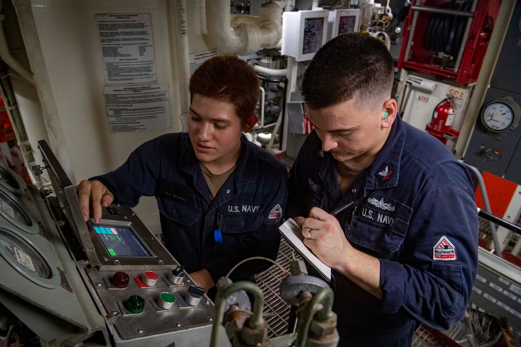 GSMFN Manuel Gutierrez, left, trains EM2 Robbie Zepponi on how to note readings on an air compressor in a main engineering space aboard USS Sterett (DDG 104) in the South China Sea.