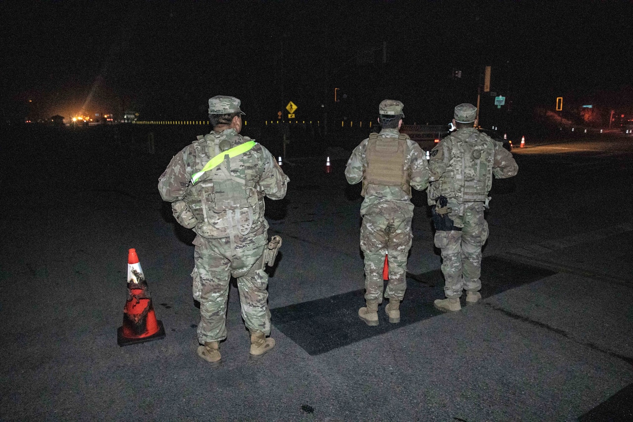 Three guardsmen stand watch over a nighttime road.