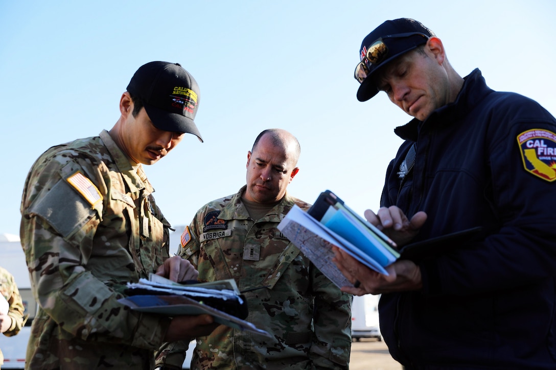 Three men in uniform huddle up at an airport with documents and talk.