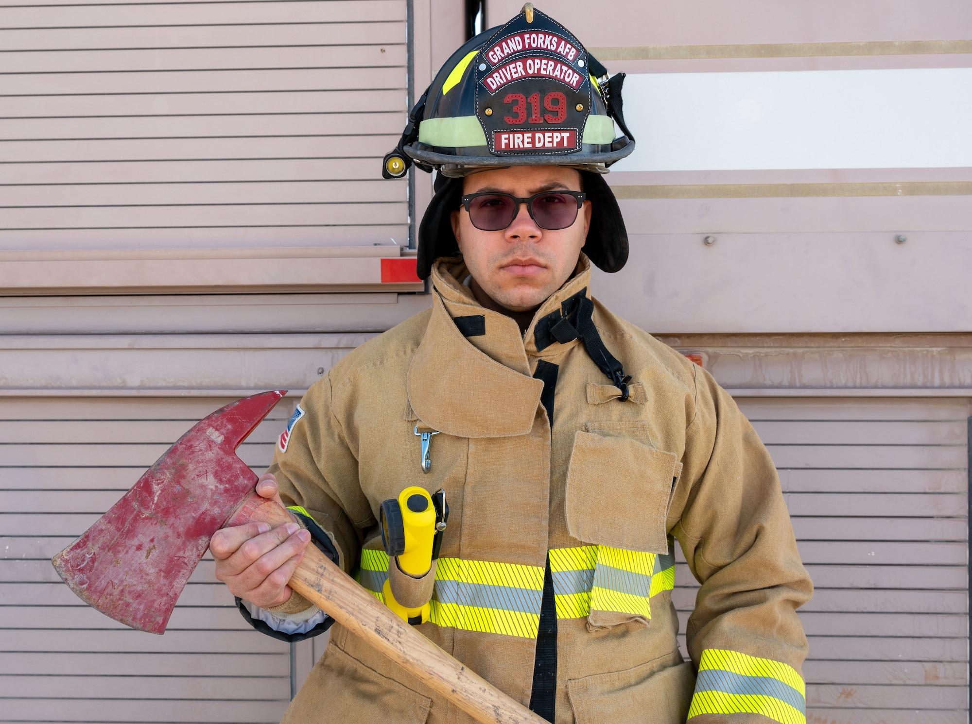 An Airman (Garcia) poses in front of a fire truck for a photo, with an axe.