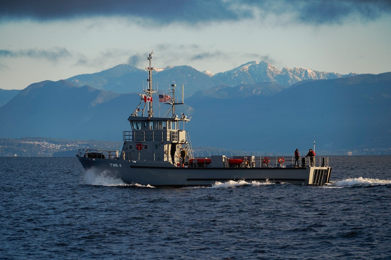 A ship plows through water with mountains in the background.