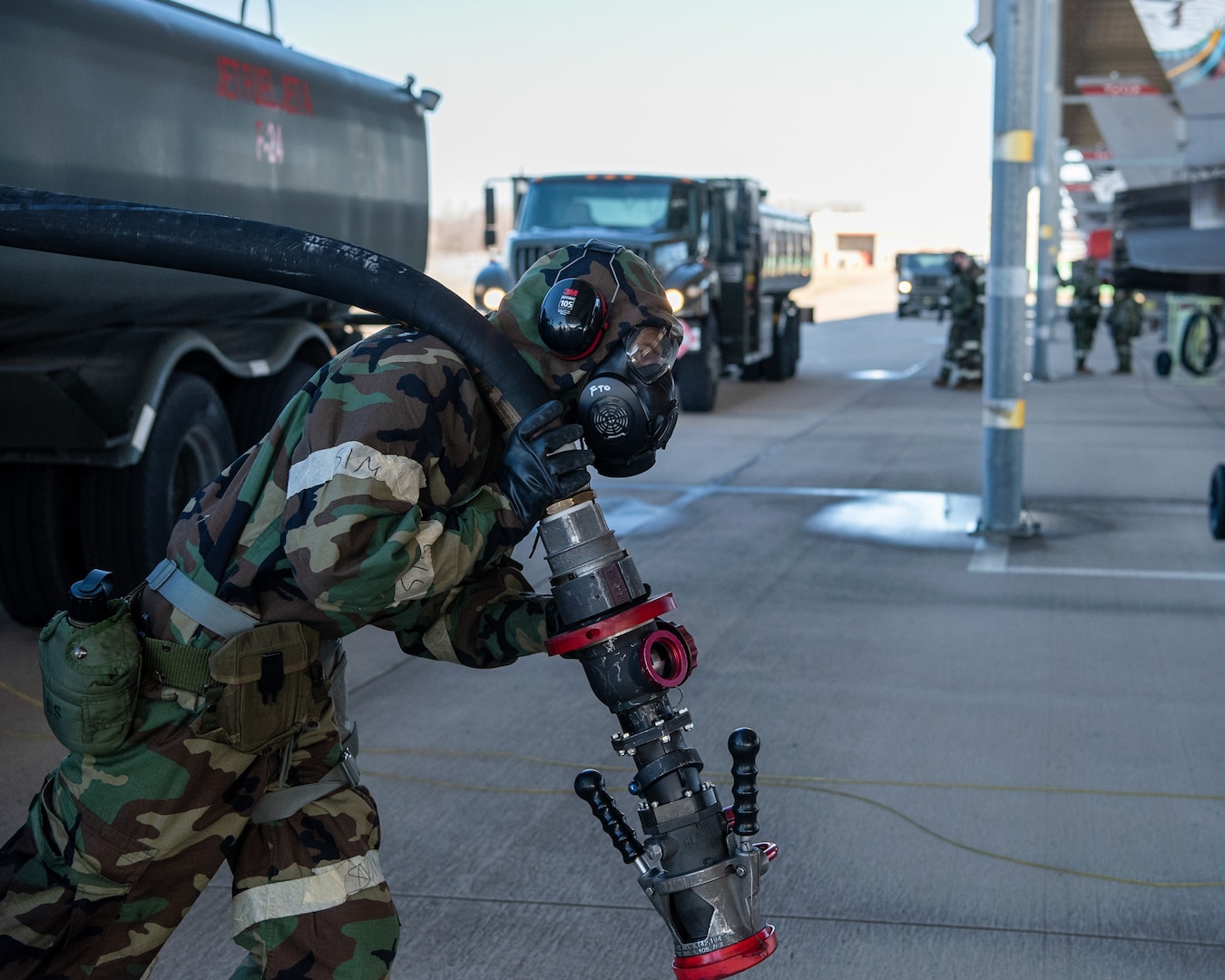 A 138th Logistics Readiness Squadron Airman hauls a gas hose to a F-16 Viper to begin refueling during a base wide exercise at Tulsa Air National Guard Base, Okla., Jan. 12, 2025. These exercises give members a chance to refresh their skills regarding the procedures of how to don their mission oriented protective posture (MOPP) gear when dealing with toxic environments that have been impacted by chemical, biological or radioactive warfare. (Oklahoma Air National Guard photo by Senior Airman Addison Barnes)