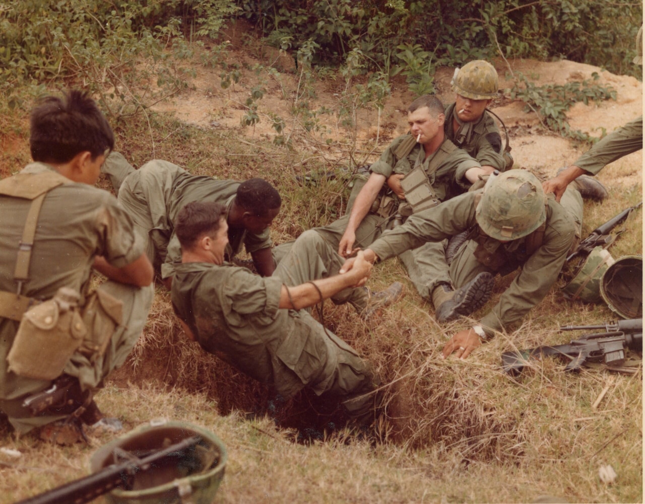 A man is lowered into a ground tunnel by a few other men.