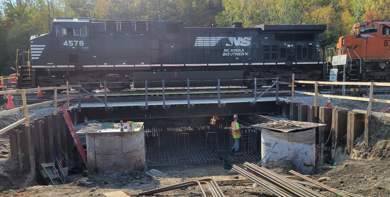 A train locomotive rolls over temporary bridge spanning construction site underneath rail tracks
